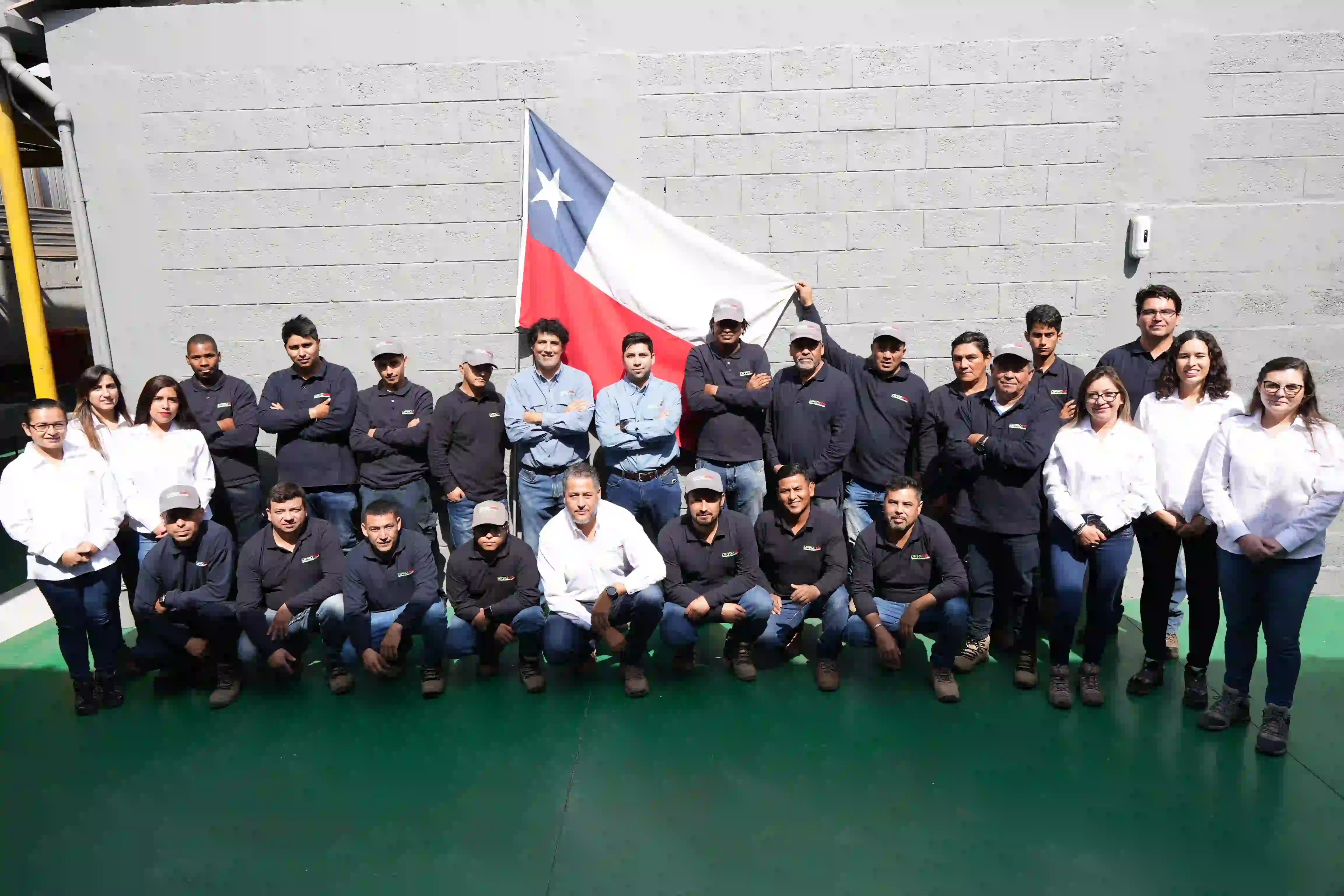 Equipo Diprofire posando frente a una pared gris, algunos de pie y otros agachados. Un miembro del equipo sostiene una bandera de Chile.