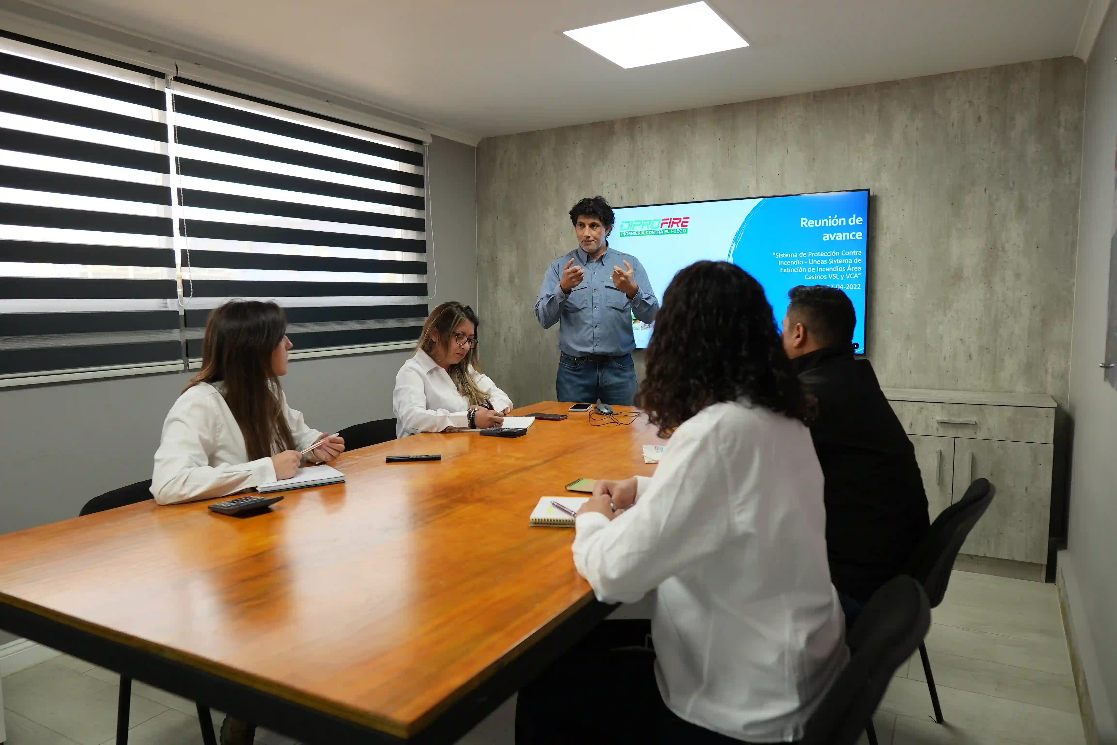 Sala de reuniones en la oficina con miembros de Diprofire sentados anotando y viendo los avances de un proyecto.